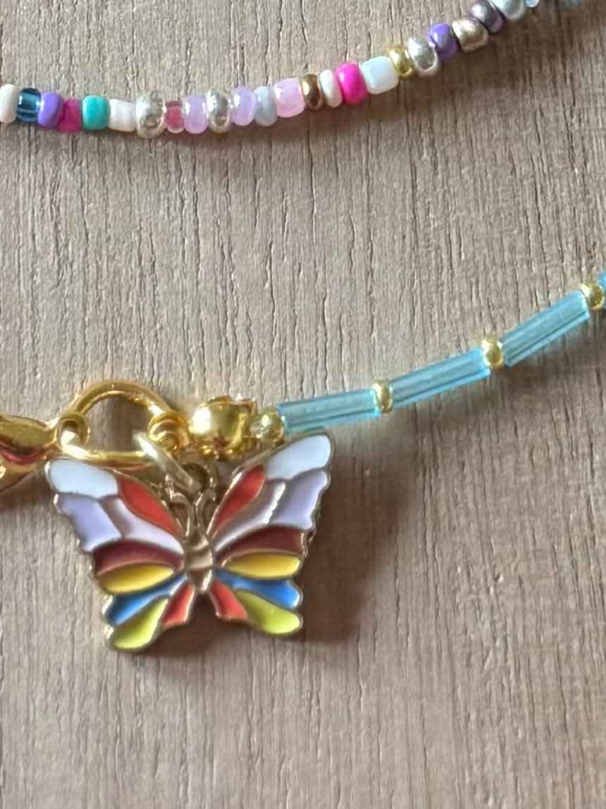 Colorful beaded necklace with a butterfly charm on a wooden surface.